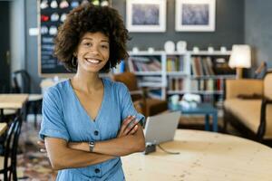 Happy young woman standing arms crossed in modern coffee shop photo